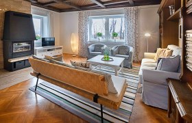 Top 1 - Wohnzimmer, © VP FeWo OG Gemütliches Wohnzimmer mit Kamin, Sofa, Sessel und Fernseher. Holzboden und Decke, gestreifter Teppich, große Fenster mit Vorhängen.