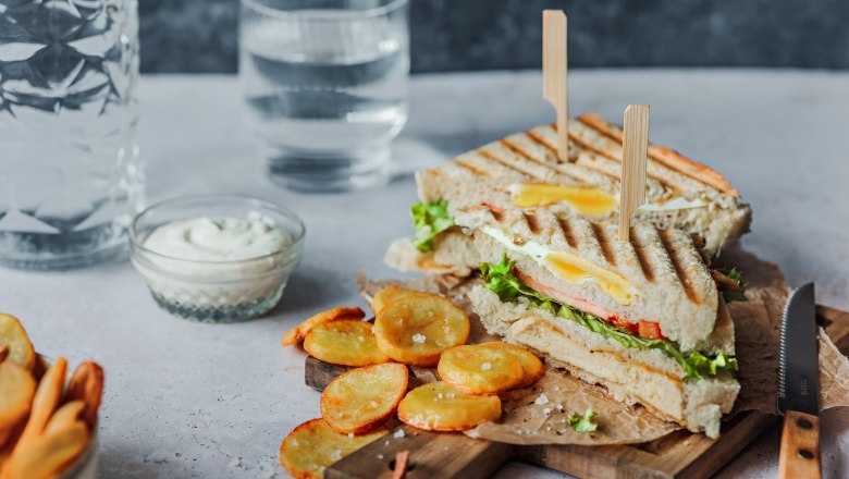 Club sandwich, © Koll GmbH A club sandwich with chips and dip on a wooden board, with a glass of water next to it.