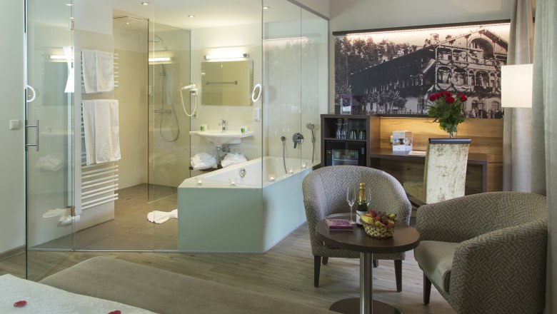 Parkzimmer Deluxe, © Hotel Schneeberghof, Robert John Luxuriöses Hotelzimmer mit Glasbad, gemütlichen Sesseln, Tisch mit Champagner und Früchten, sowie einem großen Bett mit Rosenblättern.