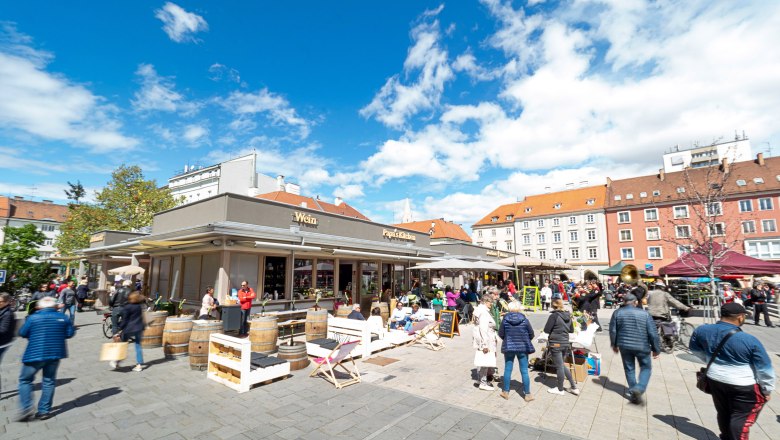 Marienmarkt, © Stadt Wiener Neustadt Michael Weller Ein belebter Marktplatz mit Menschen, die an Ständen und Cafés verweilen, unter einem blauen Himmel.