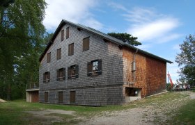 Neunkirchner Haus auf der Flatzer Wand, © Herzi Pinki Neunkirchner Haus auf der Flatzer Wand mit Holzfassade und blauen Himmel.