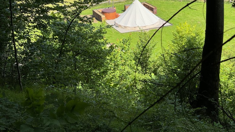 Glamping - Wildnis Zentrum Nasswald, © Jonathan Clark Blick auf ein Glamping-Zelt und einen Whirlpool auf einer Wiese, umgeben von Bäumen.