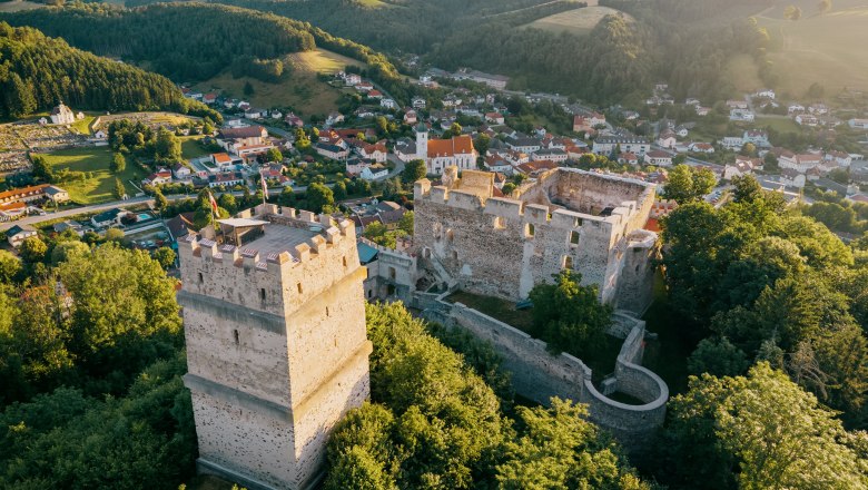 Luftaufnahme mit Feuerturm, Burgruine und dem Ort Kirchschlag, © Wiener Alpen, Roman Königshofer Luftaufnahme der Burgruine Kirchschlag umgeben von grünen Bäumen und der Stadtgemeinde Kirchschlag im Hintergrund.