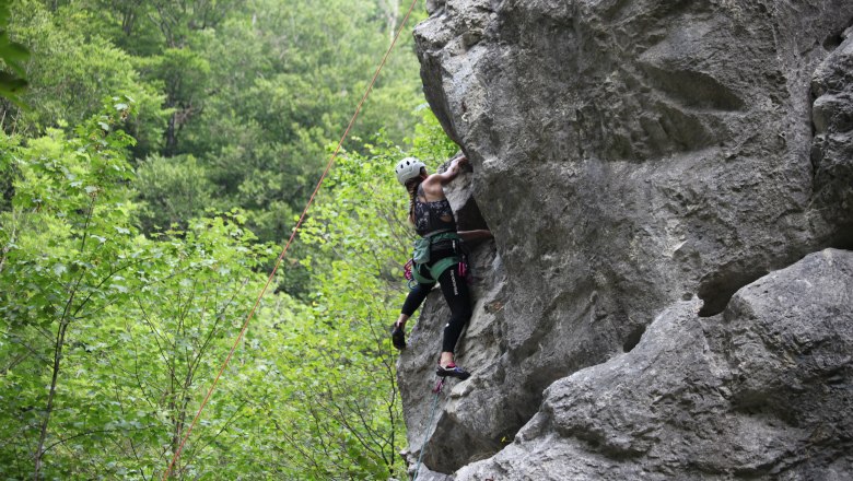 Kletter-Yoga-Camp im Höllental, © Raufgeklettert - Petra Weisz Person klettert an einer Felswand im Freien, umgeben von grünen Bäumen.