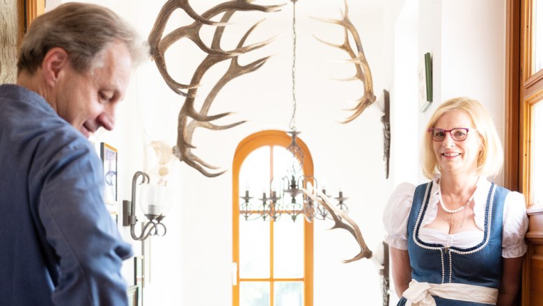 Wirtsleute Franz und Gitti Fally, © Niederösterreich Werbung/Nadja Büchler Ein Mann und eine Frau in traditioneller Kleidung stehen in einem Flur mit Geweihen an der Wand.