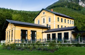 Thalhof Außenansicht, © Thalhof, Katrin Nusterer Außenansicht eines gelben Gebäudes mit Garten und Wald im Hintergrund.