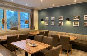 Restaurant Piestingerhof, © Wiener Alpen Innenansicht eines Restaurants mit Holztischen, gepolsterten Stühlen und einer Wand mit gerahmten Bildern.