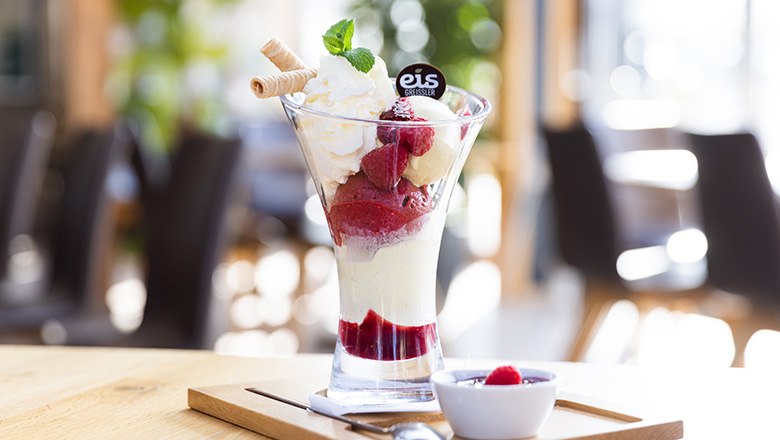 A sundae with fruit ice cream, whipped cream, waffles and raspberries on a wooden board., © Blochberger Eisproduktion GmbH A sundae with fruit ice cream, whipped cream, waffles and raspberries on a wooden board., © Blochberger Eisproduktion GmbH