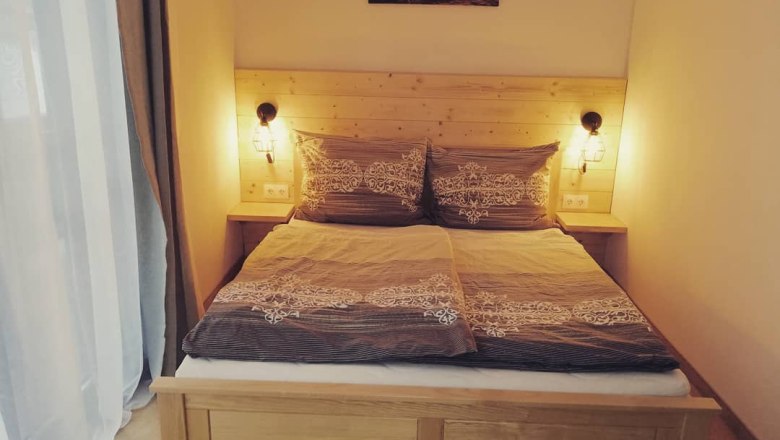 Doppelzimmer mit Ausziehcouch, © Familie Weibels Gemütliches Doppelzimmer mit Holzbett und Nachttischlampen.