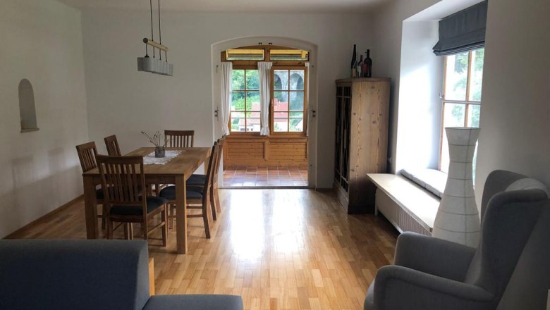 Wohnesszimmer, © Peter Wochesländer Ein Wohnzimmer mit Holzboden, Esstisch, Stühlen, Sessel und Fenster mit Blick nach draußen.