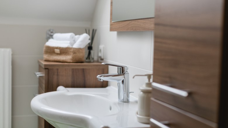 Badezimmer mit Dusche, © heiter-weiter.at/Karl Stangl Modernes Badezimmer mit Waschbecken, Holzschränken und Handtüchern in einem Korb.