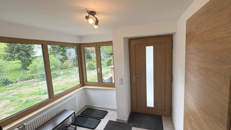 Vorraum, © Michael Hofer Heller Vorraum mit großen Fenstern, Holztür und Fliesenboden.