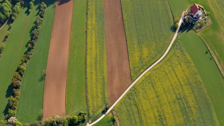 Pfarrkirche Ofenbach, © Wiener Alpen, Foto: Alois Rasinger Luftaufnahme von Feldern mit einer Kirche am Rand.