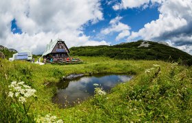 Wandererlebnis auf der Rax Wiener Alpen in Niederösterreich, Region: Semmering und Rax, © Martin Matula Umgeben von üppigen Wiesen und majestätischen Bergen, lädt die idyllische Hütte zu einer wohlverdienten Rast ein. Die klare Luft und das sanfte Plätschern des Wassers schaffen eine harmonische Atmosphäre, die Wanderer in ihren Bann zieht.