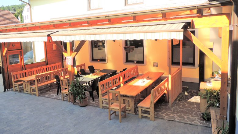 Der Gastgarten des Gasthaus Posch, © Karl Gradwohl Ein gemütlicher Gastgarten mit Holzbänken und Tischen unter einer Markise.