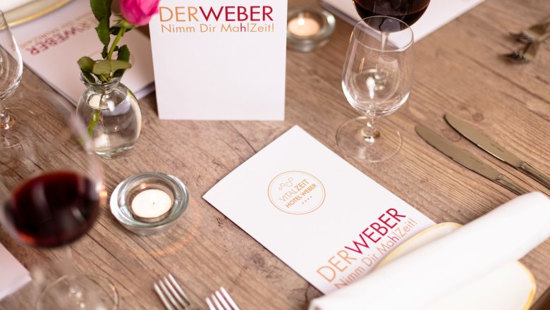 Nimm dir Ma(h)lzeit - Restaurant Der Weber, © Hotel Weber/Giefing Gedeckter Tisch im Restaurant Der Weber mit Menükarten, Weingläsern und einer Rose.