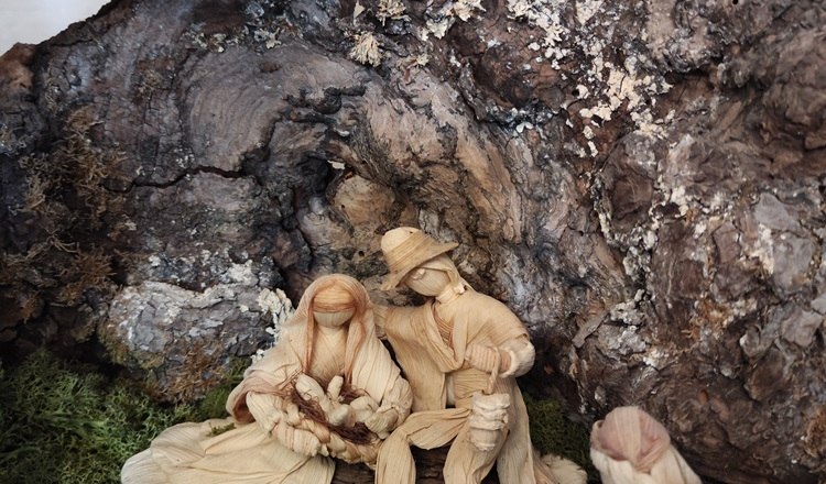 Figuren einer Naturkrippe aus Maisschalen, © Wiener Alpen Naturkrippe mit Figuren aus Maisschalen unter einem Baumstamm.