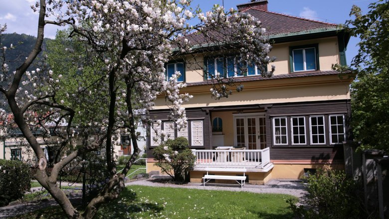 Dr. Karl-Renner-Museum, © Dr. Karl-Renner-Museum Ein zweistöckiges Haus mit Veranda, umgeben von blühenden Bäumen und einem gepflegten Garten.