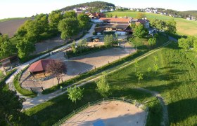 Mostheuriger Am Rosenhof - inmitten der 1000 Hügel, © Am Rosenhof - Familie Harnisch Luftaufnahme eines ländlichen Anwesens mit Gebäuden, Reitplätzen und grüner Landschaft.