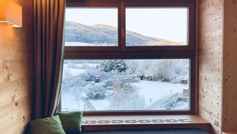 Fenster Waldtraum, © Peter Pichler Blick aus einem Holzfenster auf eine verschneite Landschaft mit Bergen im Hintergrund.