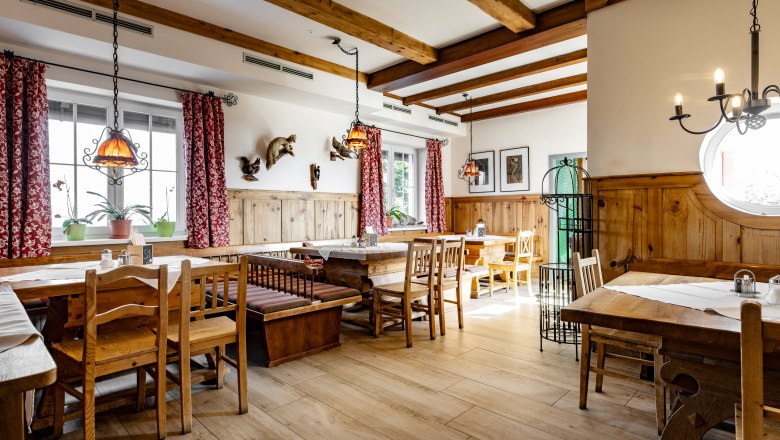 Alpengasthof Enzian, © Thomas Gobauer Cozy dining room with wooden furniture and red curtains.
