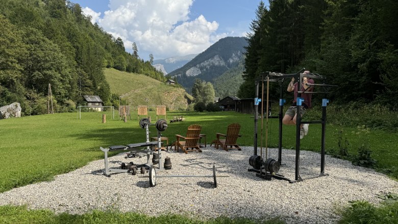 Fitness Station Wildnis Zentrum Nasswald, © Jonathan Clark Outdoor-Fitnessbereich mit Trainingsgeräten in einer grünen, bergigen Landschaft.