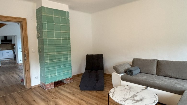 Wohnzimmer, © Michael Hofer Wohnzimmer mit grauem Sofa, rundem Marmortisch und grünem Kachelofen.