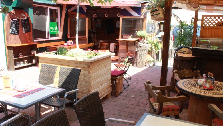 Pub garden, © Mary´s Scottish Coffeepub A cozy pub garden with tables, chairs and plants under a sun canopy.