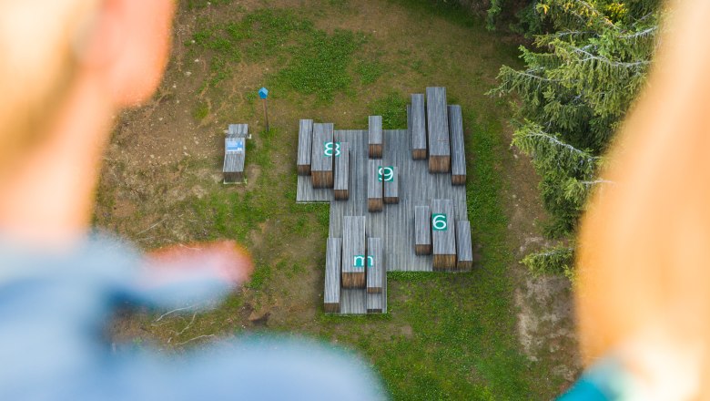 Rastplatz direkt neben der Hutwisch-Aussichtswarte, © Wiener Alpen/Martin Fülöp Blick von oben auf eine Holzplattform mit nummerierten Bänken und Tischen im Wald.