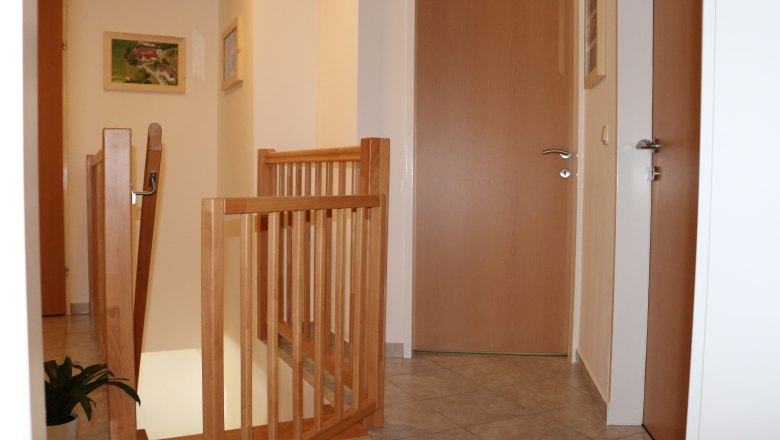 Gang 1 Gaeste 6, © Gruber Claudia Innenansicht eines Flurs mit Holztüren und Treppengeländer.