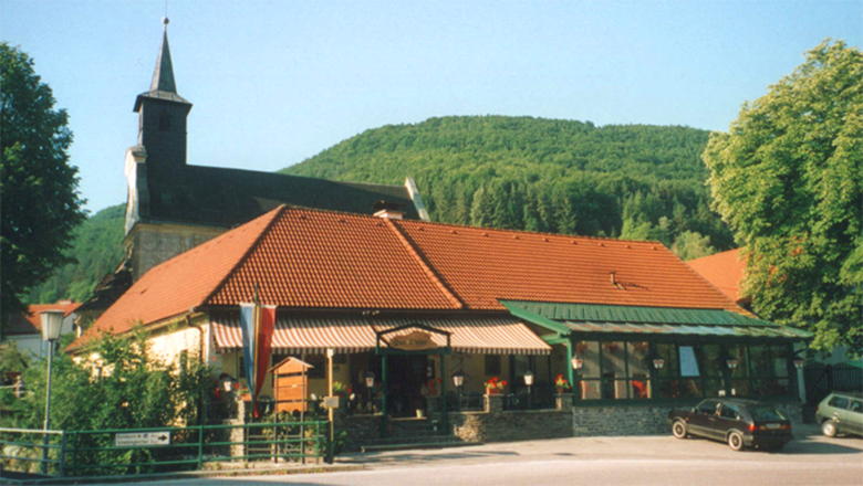 Landgasthof Thaler, © Thaler Ein Landgasthof mit rotem Dach vor einem bewaldeten Hügel.