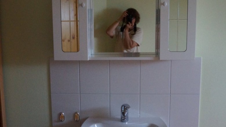 Waschbecken im Kieferzimmer, © Reep Ein Waschbecken mit Spiegel und Schrank in einem Zimmer. Eine Person fotografiert sich im Spiegel.