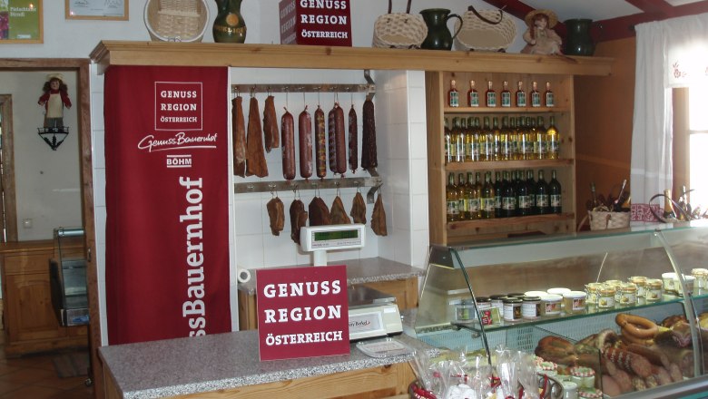 Farm store at the Böhm gourmet farm, © Genussbauernhof Böhm Interior view of a farm store with sausage products, bottles of wine and a refrigerated shelf.
