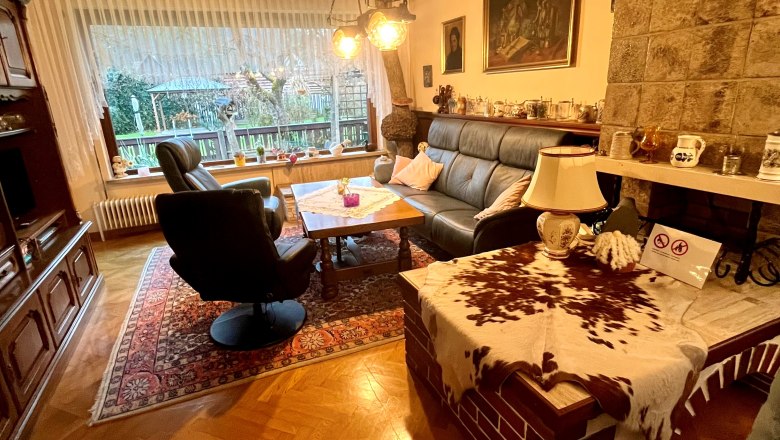 Heidis Place Wohnzimmer, © Wiener Alpen Gemütliches Wohnzimmer mit Ledersofa, Sessel, Holztisch und Kamin. Große Fensterfront mit Blick nach draußen. Rustikale Einrichtung mit Teppich.