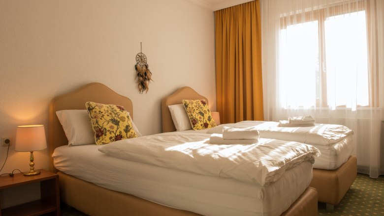 Doppelzimmer 24, © Dorfschmiede eG Ein gemütliches Doppelzimmer mit zwei Einzelbetten, gelben Vorhängen und einem Traumfänger an der Wand.