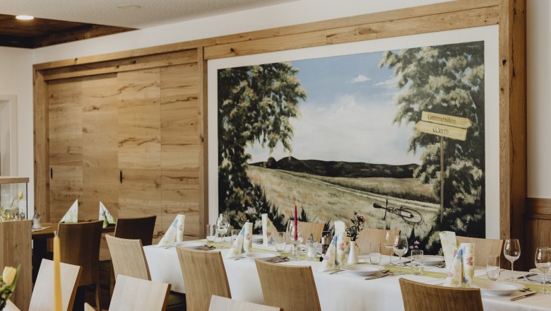 Wirtshaus in Grimmenstein, © Niederösterreich Werbung/Sophie Menegaldo Innenansicht eines Wirtshauses mit gedecktem Tisch und Wandgemälde.
