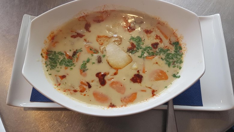 Suppen, © Reef & Beef Eine cremige Suppe mit Gemüse und Kräutern in einer weißen Schale auf einem Teller.