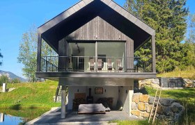 Walddenke, Hausansicht, © Mag. Plötzeneder Modernes Haus mit Holzfassade und Balkon, umgeben von Natur und einem kleinen Teich.