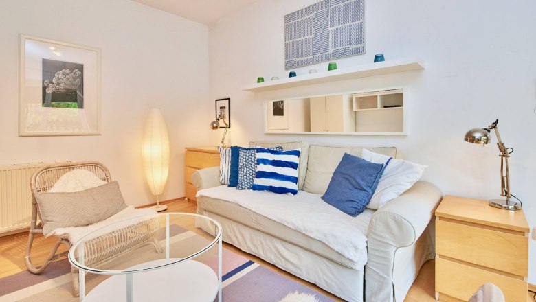 Top 2 - Wohnzimmer, © VP FeWo OG Gemütliches Wohnzimmer mit Sofa, Kissen, Sessel, Stehlampe und Couchtisch.