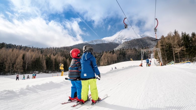 Schlepplift Losenheim - © schneebergbahn.at, © schneebergbahn.at Zwei Kinder auf Skiern nutzen einen Schlepplift in einer verschneiten Berglandschaft.