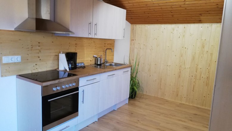 Dachgeschoss Apartment, © Familie Weibels Moderne Küche in einem Dachgeschoss mit Holzverkleidung und Geräten.