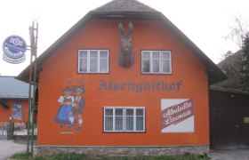 Rauraklalm, © Rauraklalm, Foto Andrea Illek Orange gestrichenes Gebäude mit der Aufschrift 'Alpengasthof', Wandmalerei von tanzendem Paar und Almdudler-Werbung.