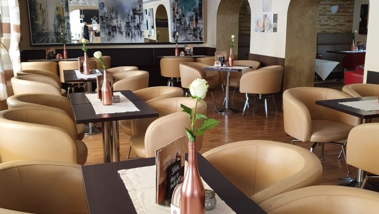 Stadtcafé Gloggnitz, © Stadtcafé Gloggnitz Innenansicht eines stilvollen Cafés mit beigen Sesseln und dekorativen weißen Blumen an der Decke.