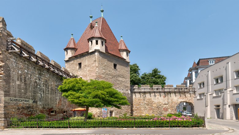Reckturm, © Wiener Alpen, Christoph Schubert Historischer Reckturm mit rotem Dach und angrenzender Stadtmauer in einer urbanen Umgebung.