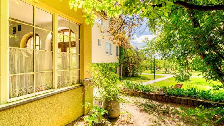 Herrenhaus Woltron, © Wiener Alpen / Christian Kremsl Ein Herrenhaus mit großen Fenstern und einem gepflegten Garten im Sonnenschein.