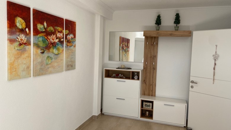 Vorraum, © Wiener Alpen Ein Vorraum mit einem dreiteiligen Seerosenbild an der Wand, einem weißen Schrank mit Spiegel und Dekorationen.
