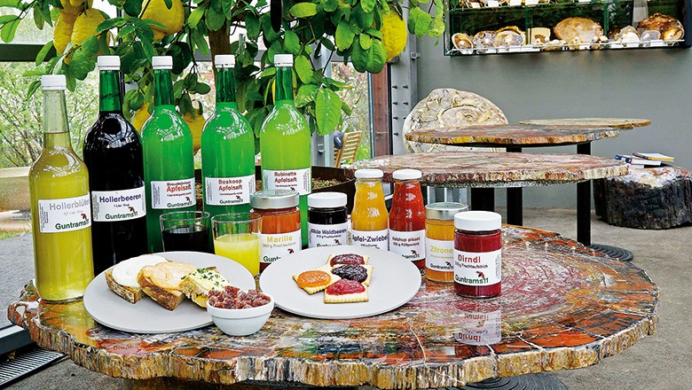 Precious wood products before the petrified wood collection, © Guntrams 11 KG Various bottles and jars of drinks and jams on a table made of petrified wood.