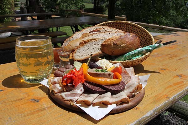 Tavern Am Rosenhof - Family Harnisch, © Am Rosenhof - Familie Harnisch Board snack with bread, sausage, bacon and drinks on a wooden table outside.