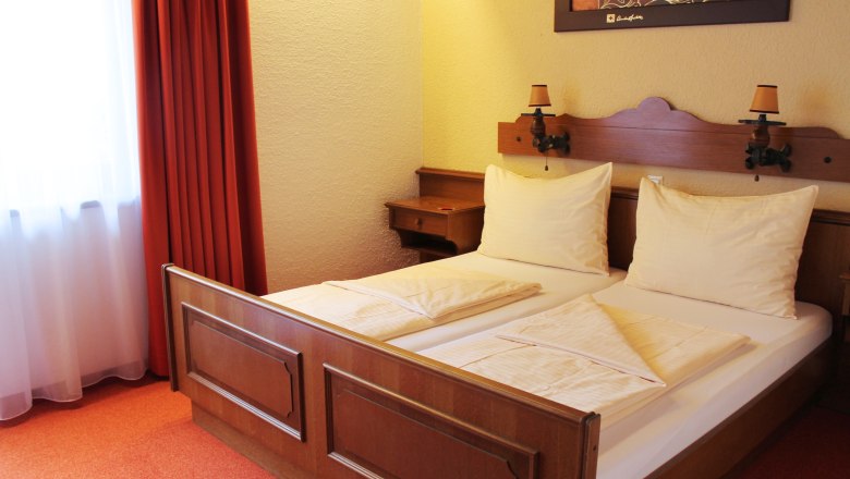 Zimmeransicht, © Tanja Schwartz Ein gemütliches Hotelzimmer mit einem Doppelbett, roten Vorhängen und einem Bild an der Wand.