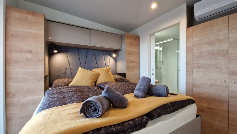 Doppelbett Johannesbachklamm Chalet, © Johannesbachklamm Chalet Modernes Schlafzimmer mit Doppelbett, gelben Kissen und Handtüchern, Holzschränken und Klimaanlage.